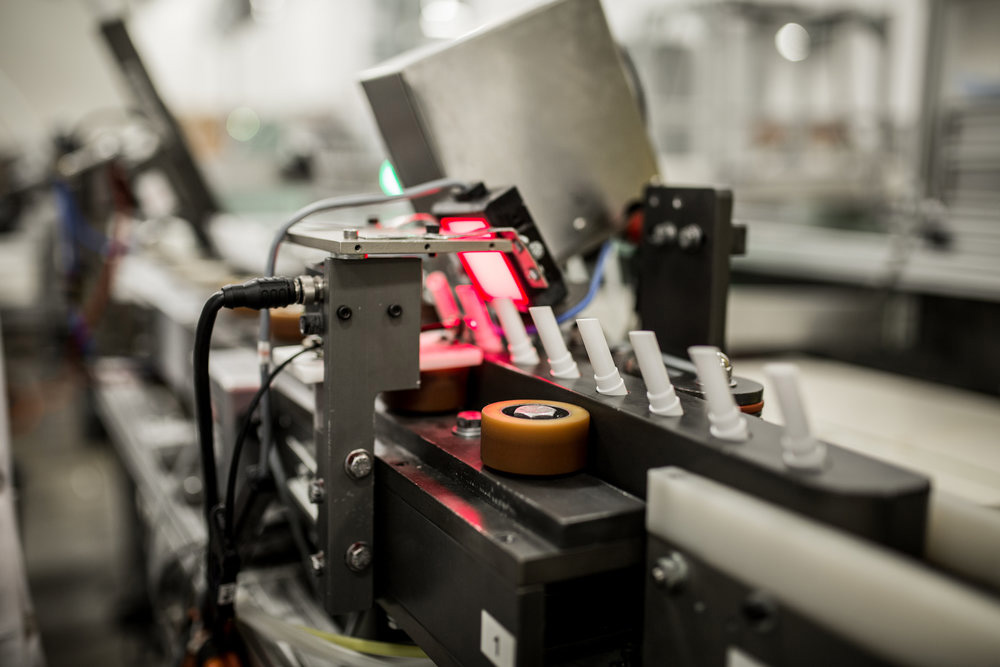 Machine processing lip balm containers on a conveyor belt in FP Labs manufacturing facility.