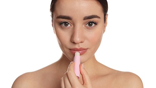 Close up of a woman applying lip balm to her lips.