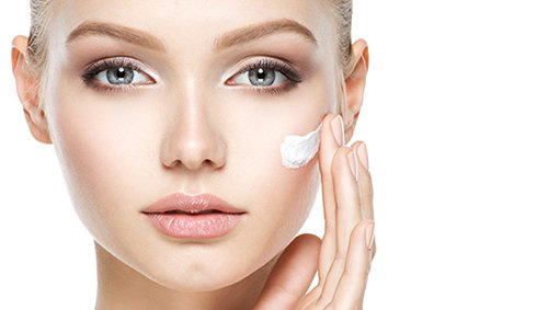 Close up of a woman applying a dab of white lotion to her cheek.