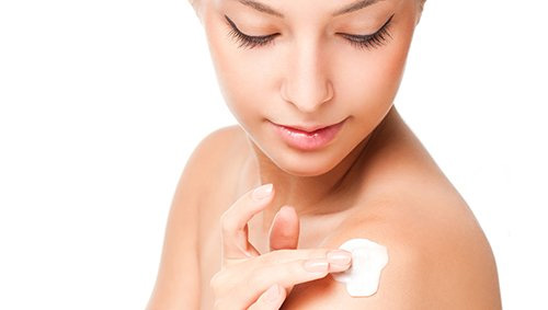 Woman looking at and applying lotion to her shoulder.