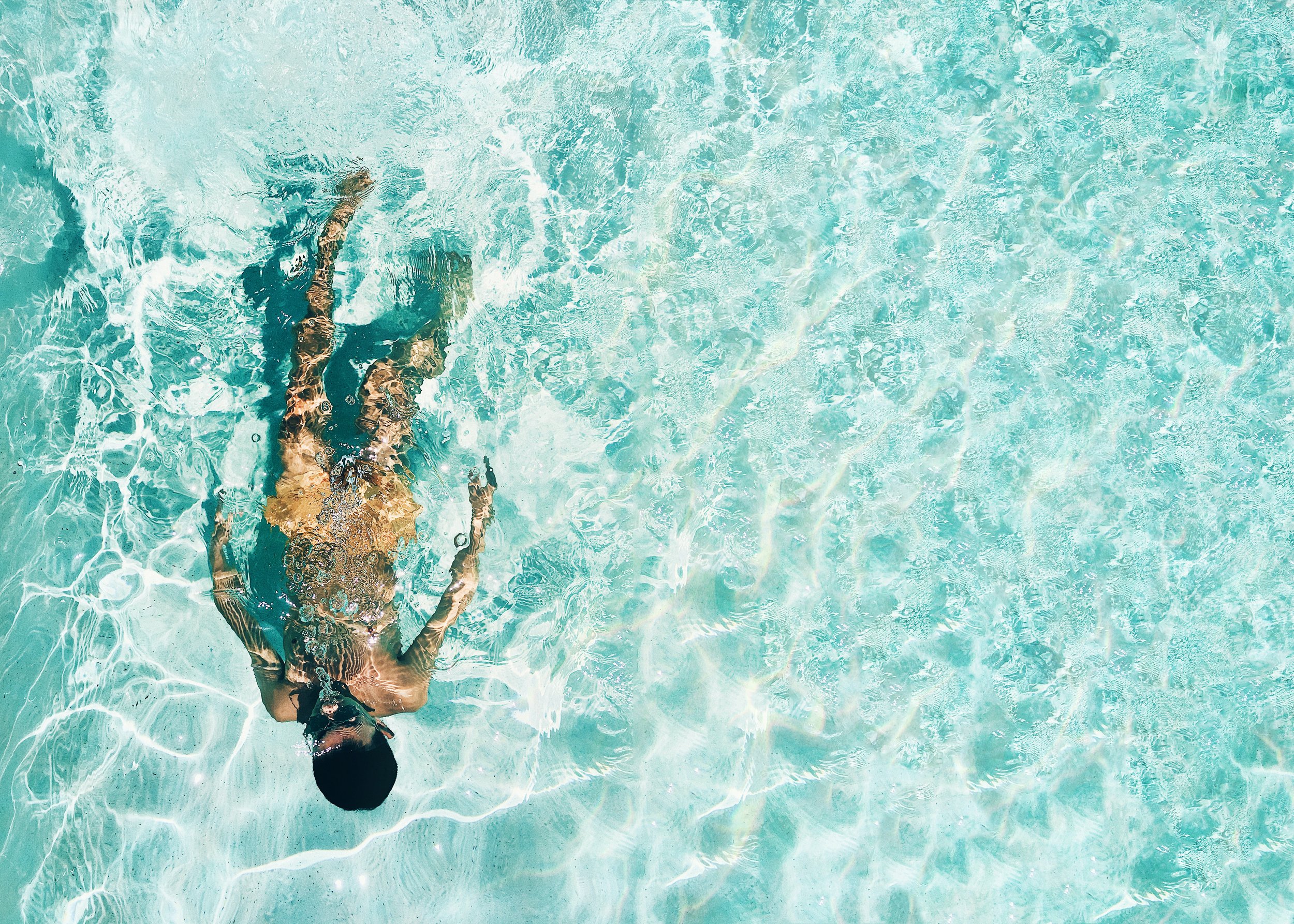 Person swimming face up in clear pool of water.