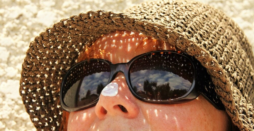 Close up of a woman's face who is wearing sunglasses and a sun hat with a smudge of sun lotion on her nose.