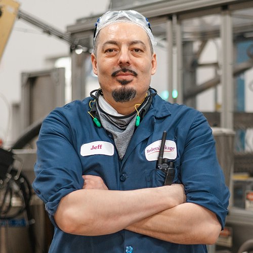 Portrait of a Jeff, a man with his arms crossed wearing goggles and a blue work shirt.