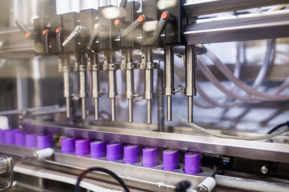 Automated machinery filling purple containers on a production line.