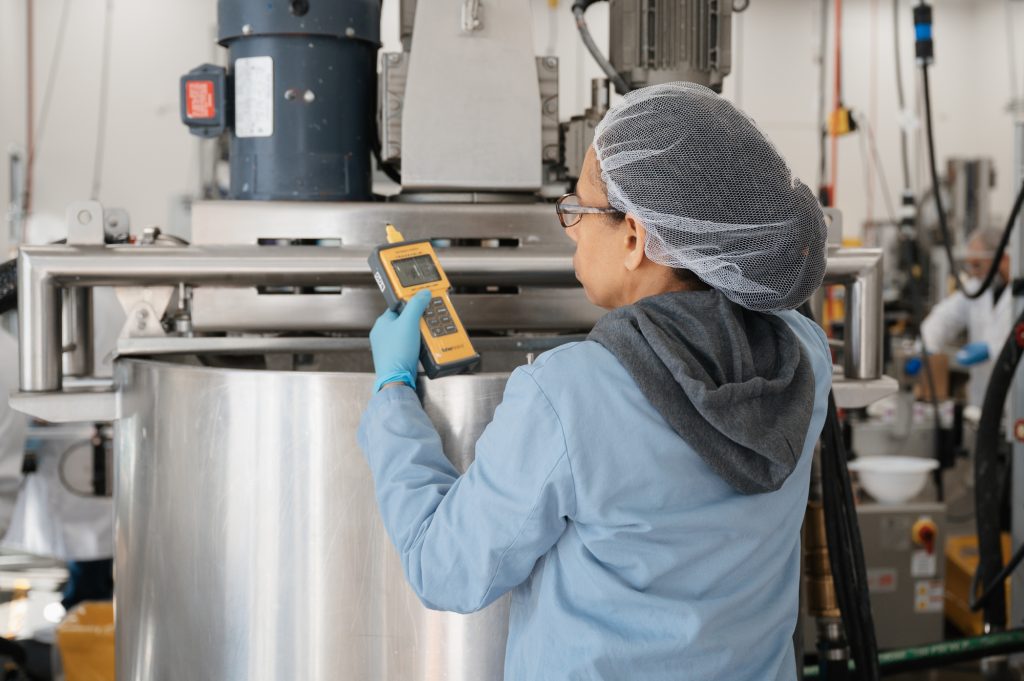 Worker in a lab coat and hairnet using a handheld device to inspect large industrial equipment in Federal Package manufacturing facility.