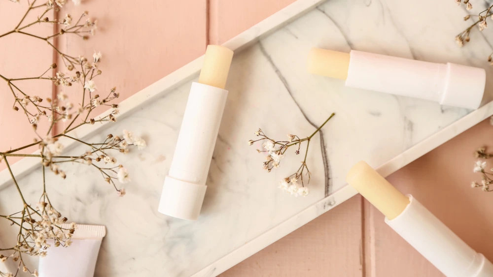 Lip balm formulation including beeswax and cocoa butter in white tubes against pink background
