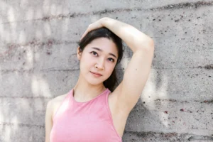 Woman in a pink tank top resting her hand on her head to show smooth, clean underarm skin, illustrating natural deodorant formulation.